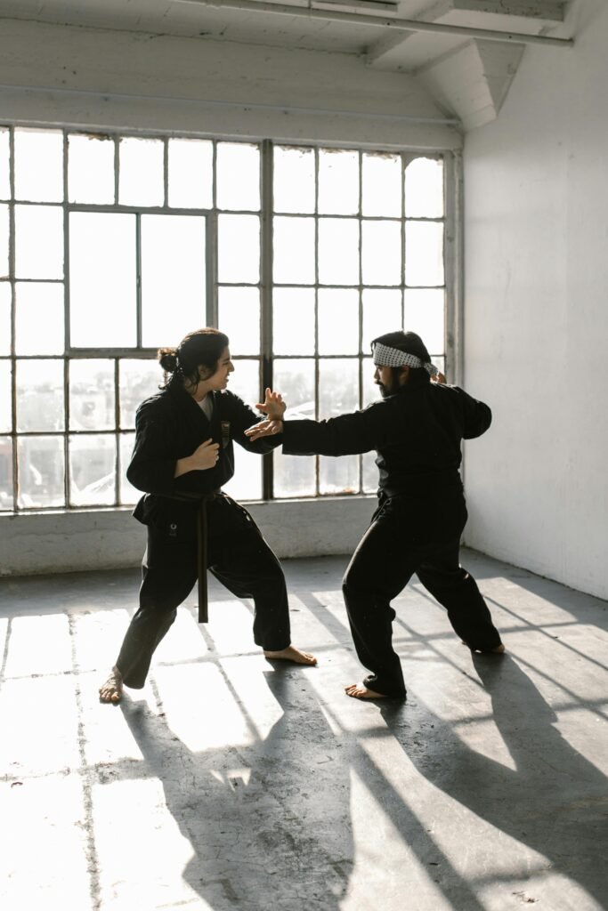 Two martial artists practice sparring in a bright, industrial-style room.