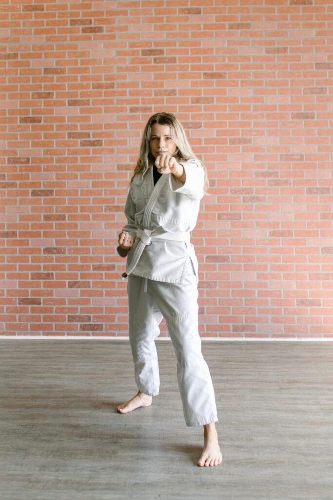 Woman in white martial arts uniform practicing taekwondo in indoor dojo.